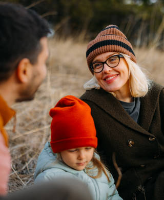 A family of three enjoys a cozy moment outdoors during an autumn vacation in the mountains. The scene captures warmth and togetherness surrounded by nature.