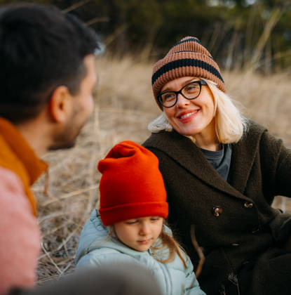 A family of three enjoys a cozy moment outdoors during an autumn vacation in the mountains. The scene captures warmth and togetherness surrounded by nature.