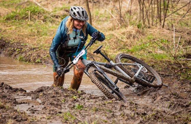 Vrouw met mountainbikefiets klautert door de modder