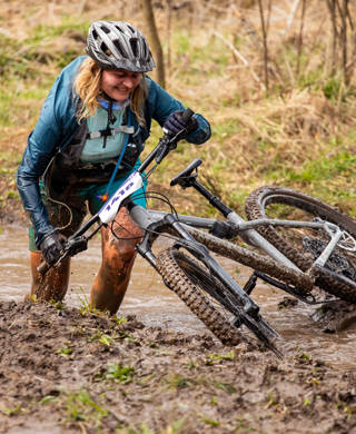Vrouw met mountainbikefiets klautert door de modder