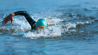 Professional triathlete swimming in river's open water. Man wearing swim equipment practicing triathlon on the beach in summer's day. Concept of healthy lifestyle, sport, action, motion and movement.