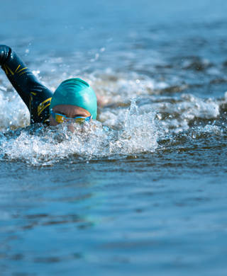 Professional triathlete swimming in river's open water. Man wearing swim equipment practicing triathlon on the beach in summer's day. Concept of healthy lifestyle, sport, action, motion and movement.