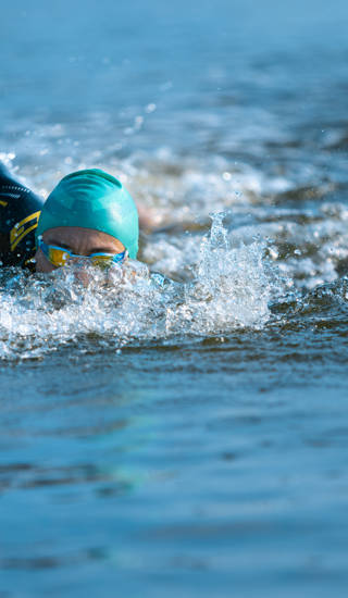 Professional triathlete swimming in river's open water. Man wearing swim equipment practicing triathlon on the beach in summer's day. Concept of healthy lifestyle, sport, action, motion and movement.