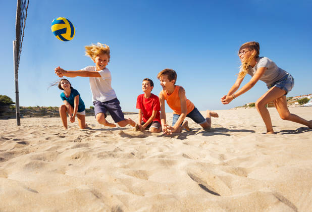 Groepje kinderen spelen volleybal op het strand, jongen slaat op