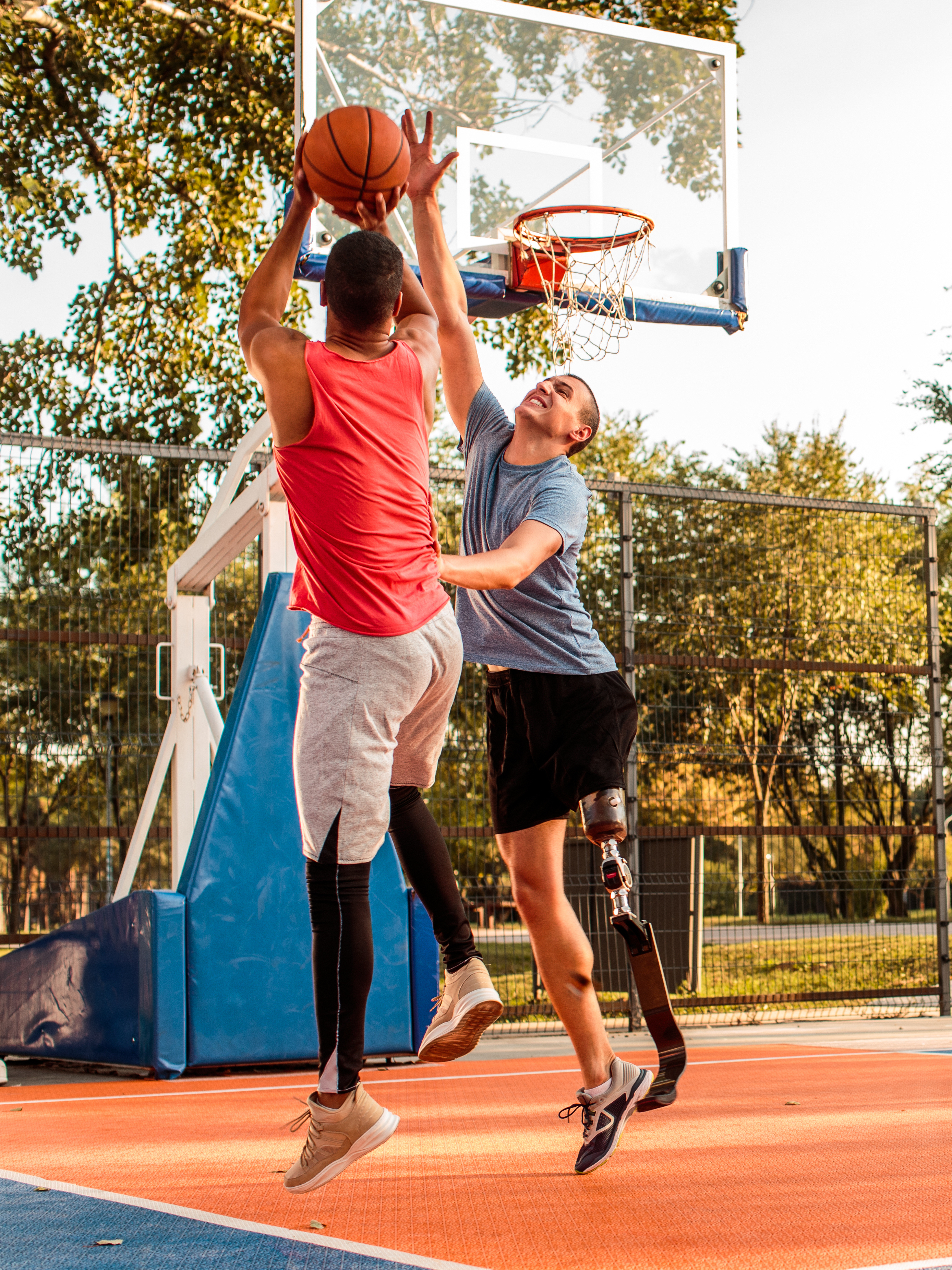 Multi-ethnic male friends playing basketball in the park. One of them has prosthetic leg.