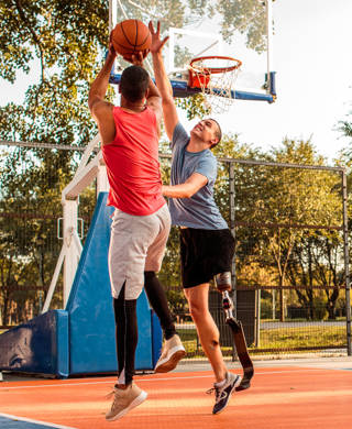 Multi-ethnic male friends playing basketball in the park. One of them has prosthetic leg.