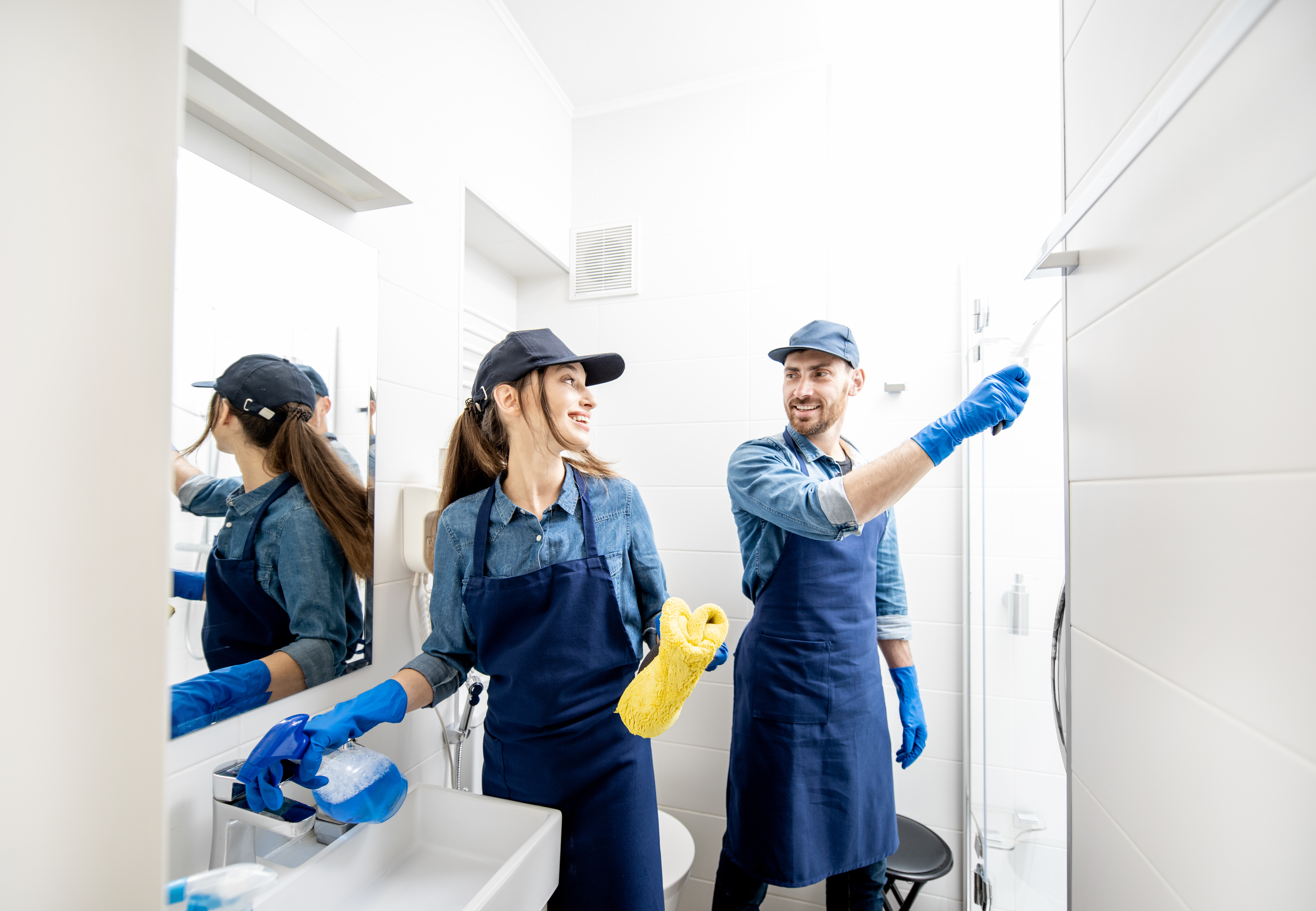 Couple as a professional cleaners in blue uniform cleaning bathroom. Cleaning service concept